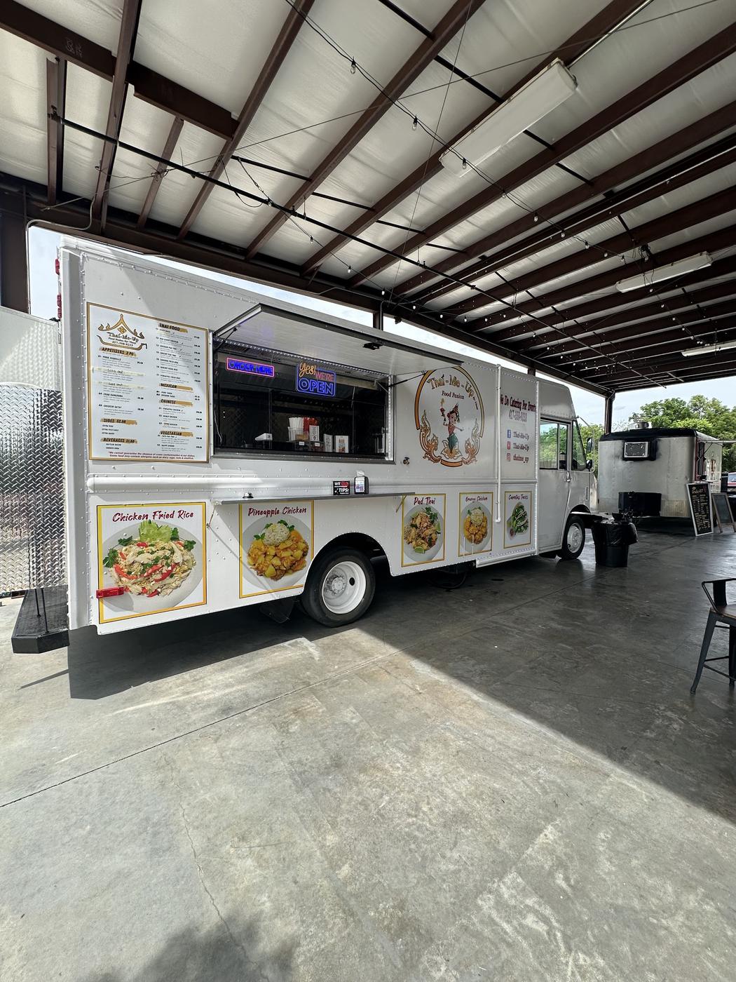 The Thai-Me-Up truck parked under a pole barn awning with its service window open